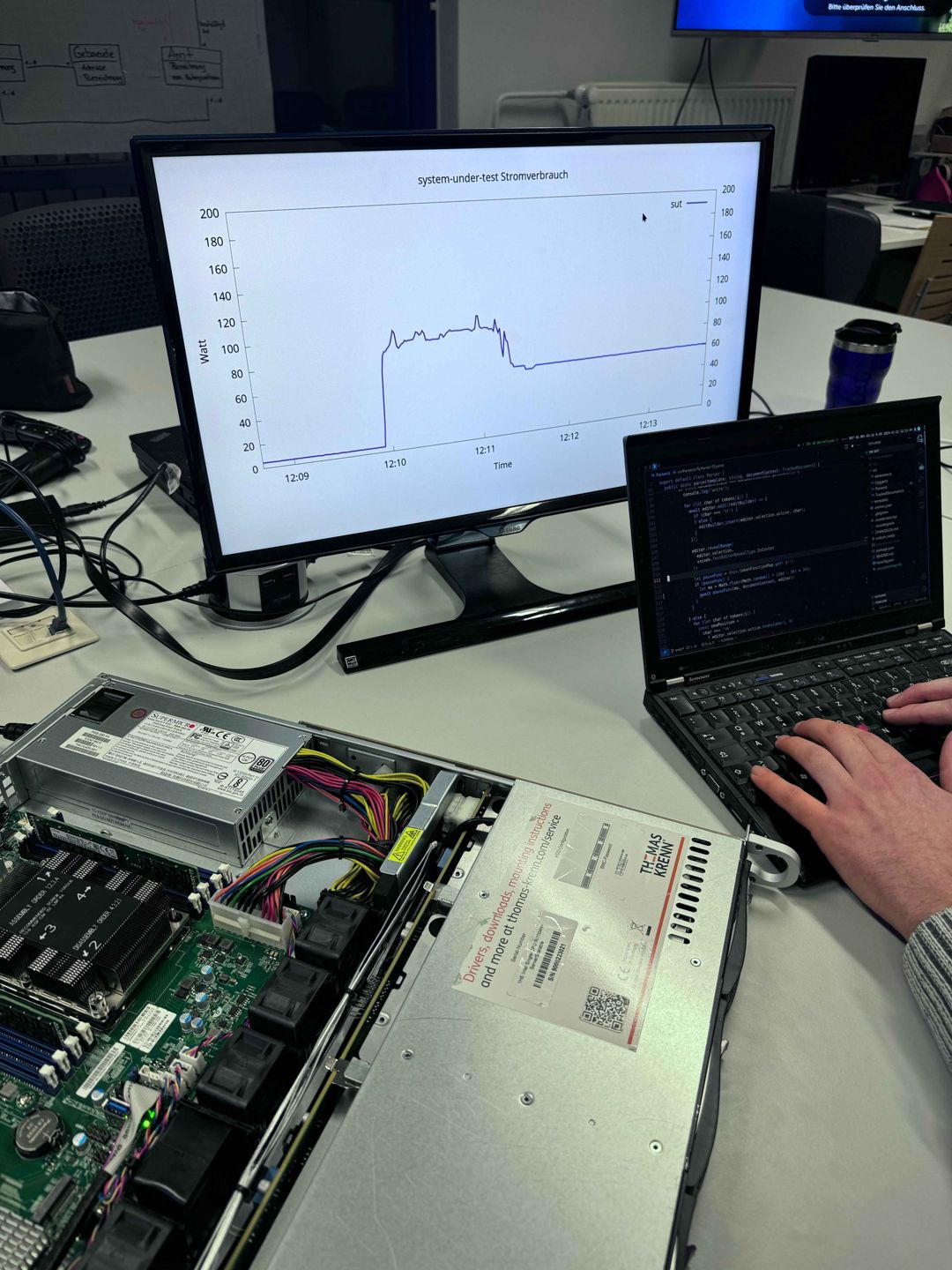 Ein Projektmitglied bei der Arbeit. Ein Server, ein Laptop und ein Monitor stehen auf dem Tisch. Auf dem Monitor wird ein Graph angezeigt.