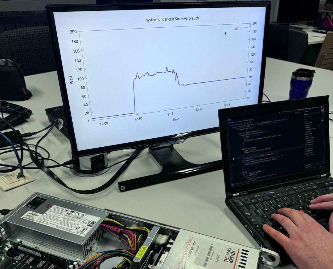 Ein Projektmitglied bei der Arbeit. Ein Server, ein Laptop und ein Monitor stehen auf dem Tisch. Auf dem Monitor wird ein Graph angezeigt.